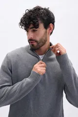 Buzo de tejido de punto en color gris, con cuello alto y cierre frontal parcial. Presenta puños y ruedo acanalados.