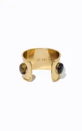 Brazalete rígido de metal dorado de banda ancha, con abertura frontal y piedras redondeadas con efecto veteado incrustadas.