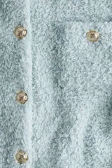 Saco corto de manga corta color celeste confeccionado en sherpa suave. Presenta cuello camisero, cierre frontal de botones metálicos dorados, bolsillos de parche en el pecho con solapa y botones, y diseño de bajo recto.
