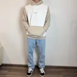 Canguro con capucha de diseño bicolor, combinando paneles en color blanco y beige. Presenta un bolsillo frontal tipo canguro y el logo de la marca bordado en el pecho.