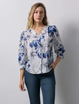 Blusa de gasa estampada con flores azules y blancas, marca Sioni. Tiene escote en V, abertura frontal con botones y mangas 3/4 con puños fruncidos y botón.