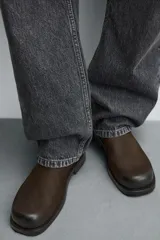 Bota de cuero color marrón oscuro con diseño de caña media, horma cuadrada y cierre lateral mediante cremallera. Cuenta con suela a contraste y un ligero tacón.