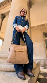Cartera de hombro color tostado, con diseño de textura sutil, bolsillo frontal con tapa y cierre, y compartimento principal con cierre superior. Incluye correa larga regulable y asas de mano.