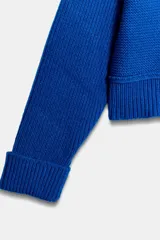 Jersey de punto color azul eléctrico con escote en pico, manga larga y detalle de costuras marcadas en los hombros. Presenta un corte ligeramente cropped con puños y ruedo acanalados.