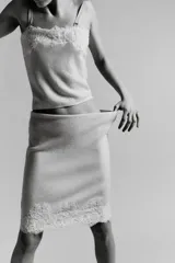 Falda midi de tejido ligero color crema o beige muy claro, con cintura elástica de color beige más oscuro. El bajo está adornado con una aplicación de encaje floral a tono.