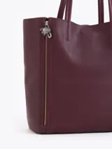 Cartera tipo shopper de cuero vacuno flor graneado, con formato amplio y estructura flexible. Presenta dos cierres verticales decorativos en el frente con tiracierres personalizados y doble manija de hombro.