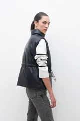 Chaleco negro de cuero sintético con cuello alto, cierre frontal con cremallera y bolsillos laterales con solapa.