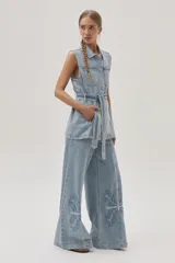 Chaleco largo de jean celeste con cuello camisero, sin mangas, con bolsillos frontales, laterales e internos, y lazo ajustable en la cintura.