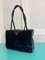 Bolso de mano o de hombro, tipo bowling o doctor bag, de color azul marino. Confeccionado en gamuza con un gran logo bordado en azul más claro en el frente. Posee dos asas trenzadas de cuero.