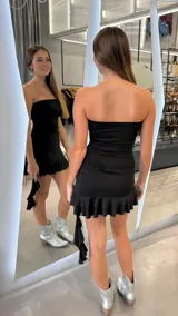 Vestido corto strapless negro ajustado al cuerpo, con diseño drapeado en los laterales y volado en el ruedo.