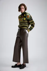 Jersey de punto con cuello subido y manga larga. Presenta un diseño de rayas horizontales en tonos verde y negro, con un panel superior decorado con calados y aplicaciones de flores tejidas en crochet de colores contrastantes.