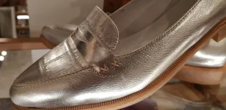 Mocasines de cuero plateado con acabado texturado, diseño clásico con costuras visibles y vira de suela natural cosida. Cuenta con taco plano de 2 cm y plantilla anatómica.