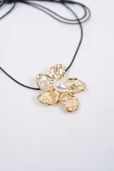 Set compuesto por un collar con cordón negro y un par de aros, ambos con dijes en forma de flor de metal plateado con textura irregular y una perla central.