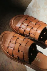 Sandalias planas de cuero con tiras plateadas tejidas en el empeine y base marrón.