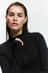 Campera deportiva negra de corte ajustado, con cuello elevado, cierre frontal y bolsillos laterales con cierre. Presenta aberturas para el pulgar en las mangas largas.