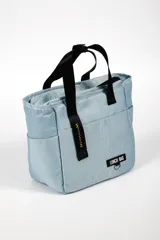 Lunchera térmica color celeste con asas cortas negras y correa larga ajustable. Tiene un bolsillo lateral y un parche con la inscripción "LUNCH BAG".