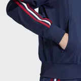 Campera deportiva Adidas Firebird azul marino con cuello alto, cierre frontal, bolsillos con cremallera y logo dorado bordado en el pecho. Presenta las tres líneas características de la marca en blanco y rojo a lo largo de las mangas.