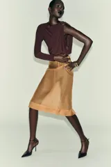 Body de manga larga color marrón oscuro, con escote asimétrico drapeado y detalle de broche metálico en el hombro derecho.