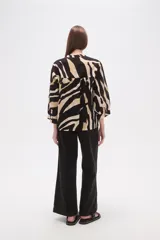 Camisa de corte holgado con estampado animal print tipo cebra en tonos negro y beige. Presenta cuello mao, cierre frontal con botones y un bolsillo aplicado en el pecho.