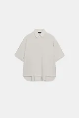 Camisa de corte fluido con cuello solapa y manga corta con dobladillo. Presenta cierre frontal con botones ocultos bajo una tapeta.