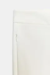 Pantalón tobillero de tiro medio, color blanco, con diseño flare o evasé en el bajo y bolsillos delanteros con cremallera oculta.