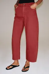 Jeans capri de tiro medio y pernera balloon, color rojo ladrillo. Confeccionados en denim, cuentan con trabillas en la cintura, bolsillos delanteros y traseros, y cierre frontal con cremallera y botón metálico.