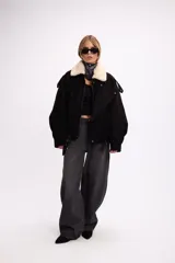 Campera de gamuza negra con cuello de piel sintética en color crema, cierre frontal, corte oversize y diseño estructurado con hombreras.