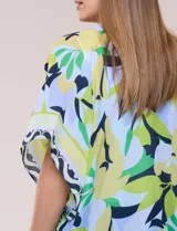 Kimono de gasa ligera con estampado floral en tonos verde, azul y celeste, de corte amplio y abierto al frente, con mangas cortas y detalle de borlas en el ruedo asimétrico.