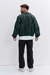 Cazadora de estilo urbano en color verde oscuro, con cuello de pana en tono marrón, cierre frontal con cremallera y puños elásticos. Presenta un diseño holgado con bordado pequeño en el pecho.