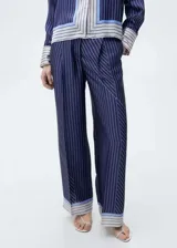 Pantalon de corte recto y diseño fluido con acabado satinado. Presenta un estampado de rayas verticales con detalles de franjas horizontales en el ruedo, cierre frontal con botón y cremallera, pinzas en la cintura y bolsillos laterales.
