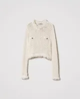 Sweater de punto calado color crema, con cuello redondo, manga larga, flecos en el ruedo y dos bolsillos de parche con botones metálicos con el logo de la marca.