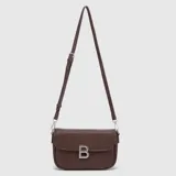 Mini cartera de cuero con textura granulada, diseño rectangular con solapa frontal y detalle de letra B metálica plateada. Cuenta con correa larga ajustable y herrajes plateados.