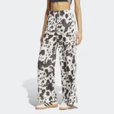 Pantalón Adidas de satén con estampado animal print tipo vaca en tonos blanco y negro, de corte holgado, perneras anchas y fluidas, cintura elástica y las icónicas 3 tiras de la marca en los laterales.
