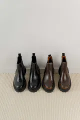 Botas tipo Chelsea de cuero con acabado vintage, diseño de caña media con paneles elásticos laterales y suela track robusta.