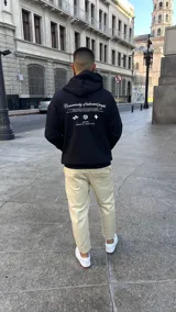 Canguro negro de corte oversize con capucha y bolsillo frontal. Presenta un estampado gráfico en la espalda con el texto 'Community of talented people' y 'SOUTH CAPITAL' junto a iconos minimalistas.