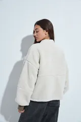 Campera de corderito color beige, con cuello camisero y cierre frontal de botones a presión. Presenta una cartera central lisa en contraste y mangas largas con puños elásticos.