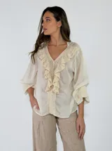 Blusa de algodón blanca con escote en V, mangas largas amplias y detalles de volados con encaje bordado en el frente.