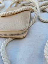 Billetera pequeña de cuero con textura efecto cocodrilo, cierre metálico perimetral y correa de muñeca extraíble. Incluye detalle de moneda metálica decorativa.