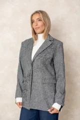 Blazer de corte sastre con diseño de espiga en tonos grises. Presenta un bordado floral lineal en el lateral, solapas clásicas, cierre frontal con un botón y bolsillos con solapa.