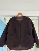 Campera acolchada color chocolate con diseño matelaseado en forma de rombos, cuello redondo y dos bolsillos frontales. Presenta un corte holgado con ruedo redondeado.
