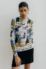 Top de manga larga y cuello alto, confeccionado en microtul con estampado abstracto en tonos azules, amarillos, morados y negros sobre fondo blanco.