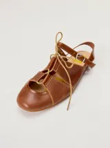 Sandalias planas tipo slingback de cuero marrón, con diseño delantero calado, cierre de cordones y tira trasera ajustable con hebilla.