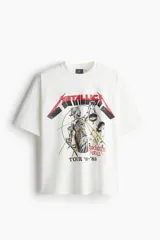 Remera de algodón color blanco crudo, corte oversized y manga corta. Presenta un estampado frontal grande con el logo de Metallica y la ilustración de Lady Justice, con el texto "AND JUSTICE FOR ALL" y "TOUR '83-'89".