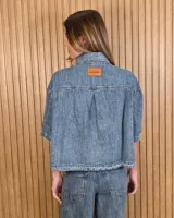 Sobrecamisa de denim soft azul, con cuello clásico, mangas cortas amplias, bolsillos frontales con solapa y cierre de botones metálicos.