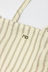 Bolso tipo tote bag de tela con diseño de rayas verticales en tonos beige y gris, decorado con volados en los laterales y la base. Incluye dos asas largas para llevar al hombro y una etiqueta con logo en el frente.