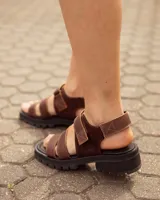 Sandalias de cuero color marrón chocolate, con tiras en el empeine, suela flatform track negra y tira con cierre ajustable en el talón.
