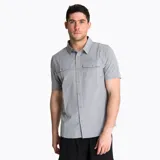 Camisa de manga corta Merrell, color gris cemento, con cuello clásico, cierre frontal de botones y dos bolsillos frontales con solapa en el pecho. Presenta un diseño funcional con tejido técnico transpirable.