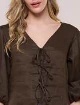 Blusa color beige confeccionada en lino, con escote en V pronunciado y cierre frontal de múltiples lazos para atar. Presenta mangas abullonadas tres cuartos con puños elásticos y corte relajado.