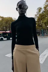 Pantalón tipo culotte de tiro alto, con pernera ancha y corta. Presenta detalles de botones dorados decorativos en la parte frontal y cierre lateral con cremallera oculta.