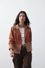 Blazer de gamuza color terracota con bordados decorativos en color crudo en solapas, puños y ruedo. Presenta corte recto, solapas clásicas y cierre frontal con un botón forrado.
